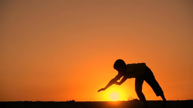 Silhouette of boy standing somersault against sunset