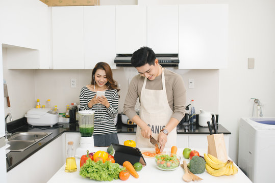 Asian woman using cell phone while a man prepares a meal
