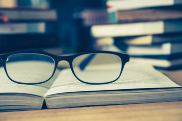 Close up of open book with eyeglasses on wooden desk, Soft focus, Vintage tone