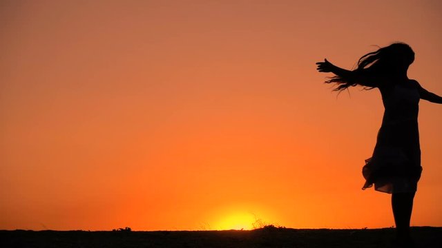 Silhouette of young girl dancing at sunset