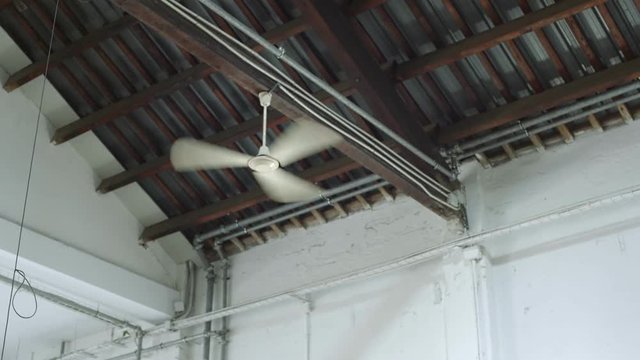 Fast rotating blades or air conditioning ventilator or fan attached to metal ceiling of industrial building with white walls, concept heat, summer. cold wind