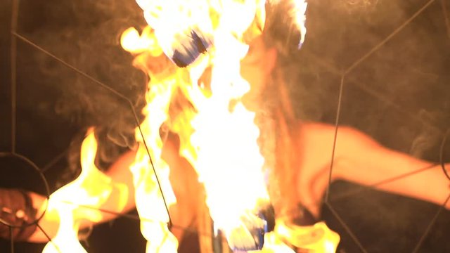 Young girl with beautiful eyes dances with burning torches made in shape of fans at fire show.