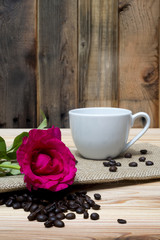 Fototapeta na wymiar Pink rose coffe cup and coffee beans on wooden table