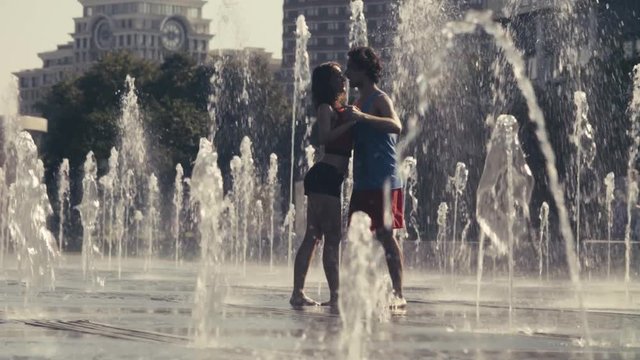 Young happy couple dancing in the fountain
