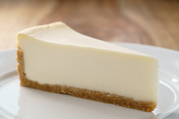 slice of traditional new york cheesecake on white plate on wood table