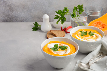 Pumpkin soup with cream and parsley on a grey concrete or stone background, selective focus, copy space