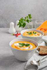 Pumpkin soup with cream and parsley on a grey concrete or stone background, selective focus, copy space