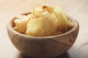 toned photo of potato chips with herbs in wood bowl on rustic table