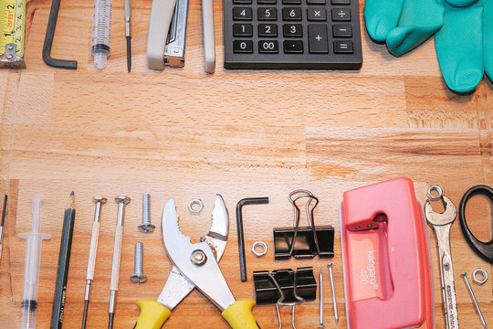 A set of tools , calculator,spanner,screw driver,rubber glove,stappler,pape clip and paper puncher on the wooden board.