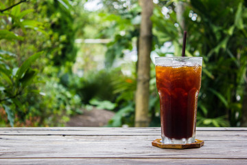 Ice coffee on wood table with green nature background. Copy space.