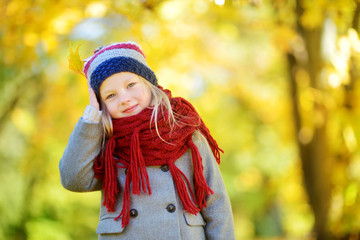 Cute little girl having fun on beautiful autumn day. Happy child playing in autumn park. Kid gathering yellow fall foliage.