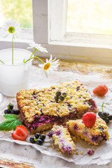Black currant, strawberry and cottage crumble cake on baking paper and rustic background