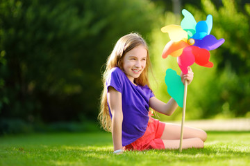 Adorable little girl holding colorful toy pinwheel on sunny summer day