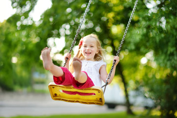 Cute little girl having fun on a playground outdoors on warm summer day
