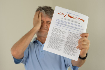 Angry upset man holding out his hand to show the jury duty summons he received in the mail which means he must be a juror on a court case. - 169321398
