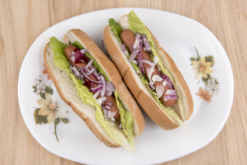 Two hot dogs with lettuce and red onions on a white plate