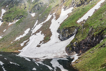 Nature landscape, shore of glacier lake Balea and Fagaras mountains with white spots of snow at Carpathians, Romania