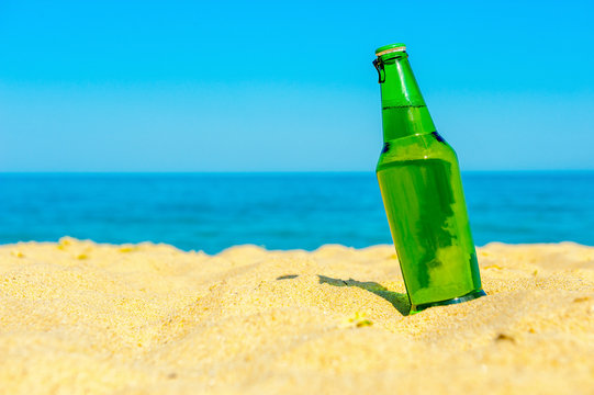 bottle of fresh beer costs on the beach in sand, on a background the sea