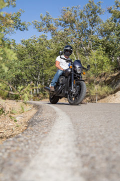 Front view of man sitting on parked custom motorcycle on road in mountains. 