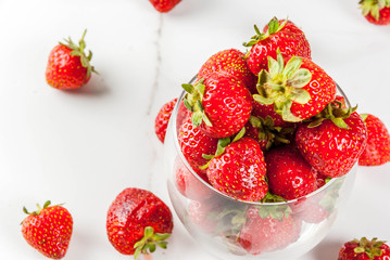 Summer berries and fruit. Fresh raw organic strawberry in drinking glass on white marble table, copy space