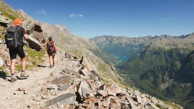 Couple hiking on footpath in idyllic mountain landscape with blue lake, high mountain peak and glacier. Summer adventures on the Alps.