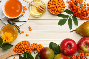 Sea buckthorn in wooden bowl, honey, rowan, apple, pear on wooden table. top view with copy space