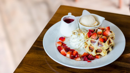 Waffle strawberry with vanilla ice cream on the table with blurry background inside coffee shop