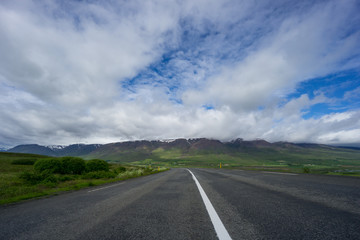 Iceland - Highway curve in front of majestic green mountain chain