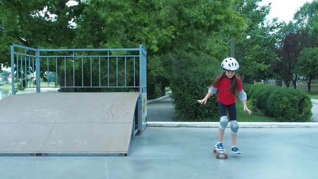 The child learns to skate. Little girl in helmet and defense on skateboard.