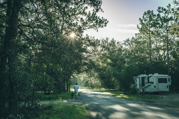 man walking a dog past an RV at a Central Florida camp ground on an early summer morning