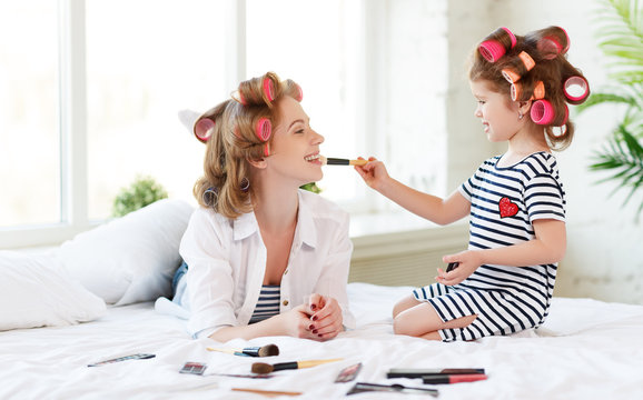 Mother and baby daughter in curlers  doing makeup on bed
