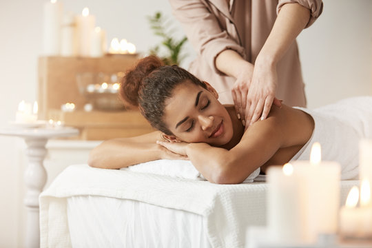 Tender african girl smiling enjoying massage with closed eyes in spa resort.