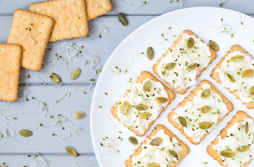 Tasty crackers with cream cheese, seeds and greens. Appetizers on a plate on grey table. Healthy...