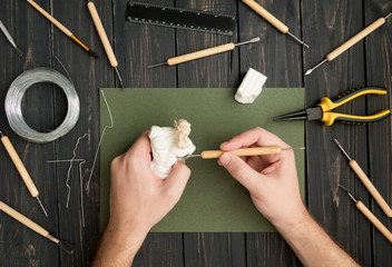 Craftsman hands working on orc sculpture, sculpturing from polymer clay against working table with...