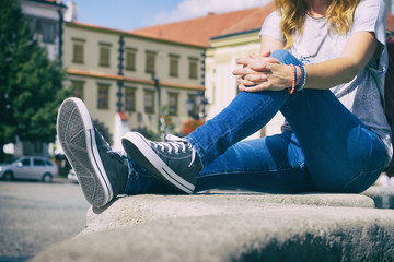 Young girl sitting on city fountain dressed in jeans and sneakers 