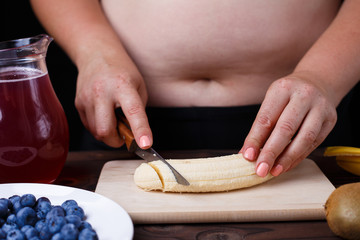 Overweight fat woman slicing a banana for fruit plate. Juicy tasty low-calorie dessert for weight losing, dieting, healthy food, well-being.