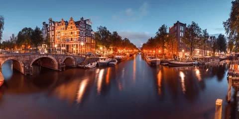 Plexiglas foto achterwand Panorama van Amsterdamse gracht, brug en typische huizen, boten en fietsen tijdens avondschemering blauw uur, Holland, Nederland. Gebruikte toning © Kavalenkava