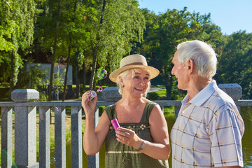 Fototapeta premium Old couple with bubble blower. Senior people, summer park background. Why having fun is important.