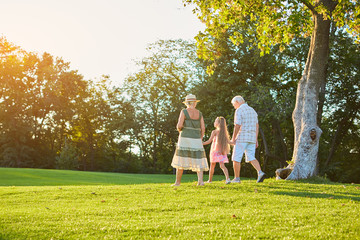 Grandparents and grandchild walking outdoors. People, sunny summer day.