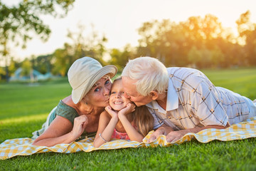 Grandparents kissing happy granddaughter. Child smiling outdoors. Taking care of grandchildren.