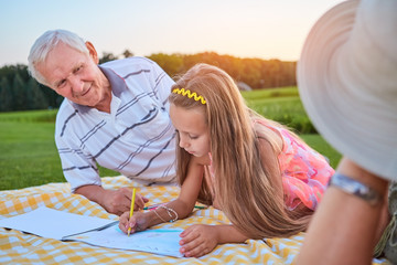 Fototapeta premium Girl with pencil drawing outdoors. Grandpa looking at granddaughter.