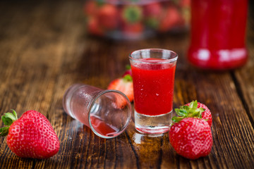 Portion of Strawberry liqueur on wooden background, selective focus