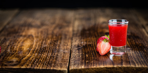 Portion of Strawberry liqueur on wooden background, selective focus
