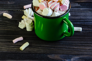 The green enameled mug is filled with a multicolored marshmallow on a black wooden table top view