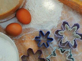 Snowflake shape cookies cutters, eggs, flour in a bowl, linen napkin on vintage wooden board for...