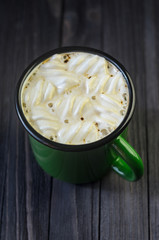 Hot drink with white marshmallows in a green enamel mug on a black wooden table top view. Dark wooden background. Space for text.