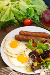English breakfast - toast, egg, sausages and vegetables salad. Wooden rustic background. Close-up. Top view