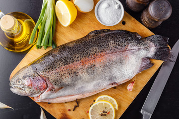 Trout spent raw on a cutting wooden board with spices, herbs, salt and olive oil. Top view