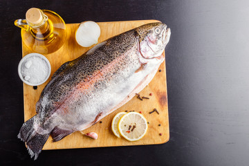 Gutted trout on a wooden cutting board with ingredients for cooking. Top view