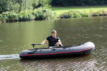Fototapeta na wymiar Junger Mann im Schlauchboot mit elektrischem Außenborder fährt am Fluss.